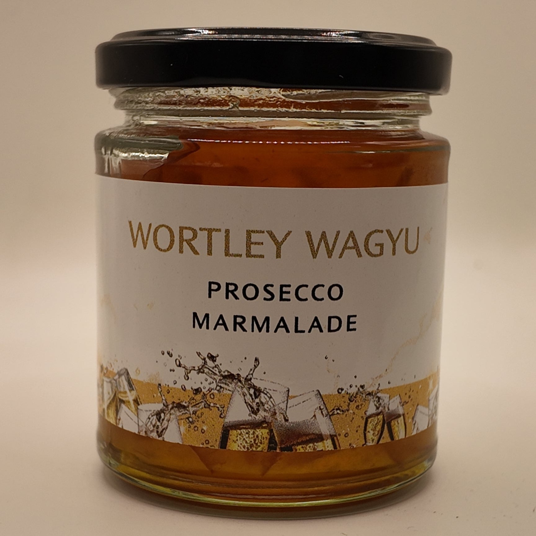 A glass jar of Wortley Wagyu Prosecco Marmalade with a black lid and a white label, set against a plain beige background.