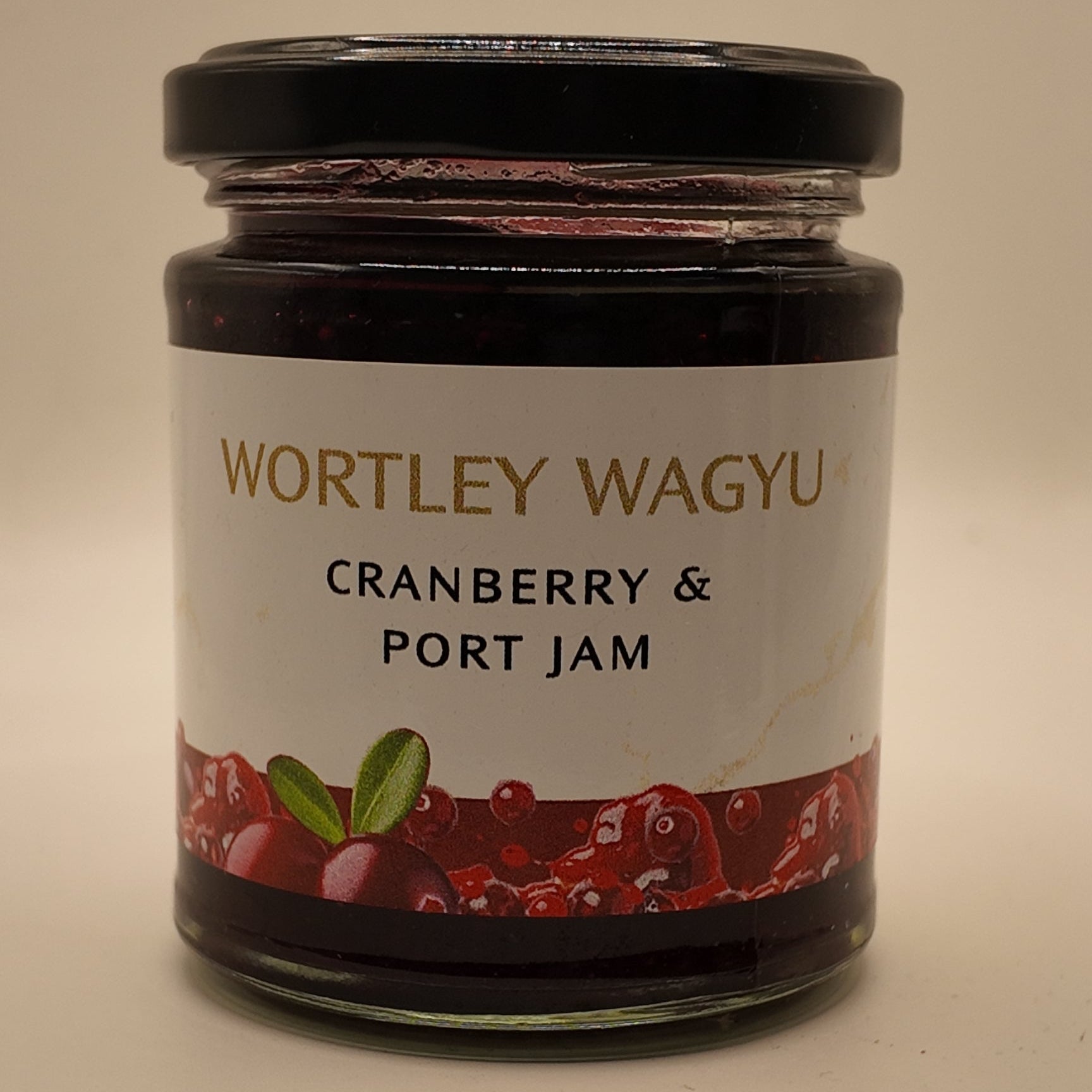 A glass jar of Wortley Wagyu Cranberry & Port Jam with a black lid and a white label featuring red cranberry illustrations, set against a plain beige background.