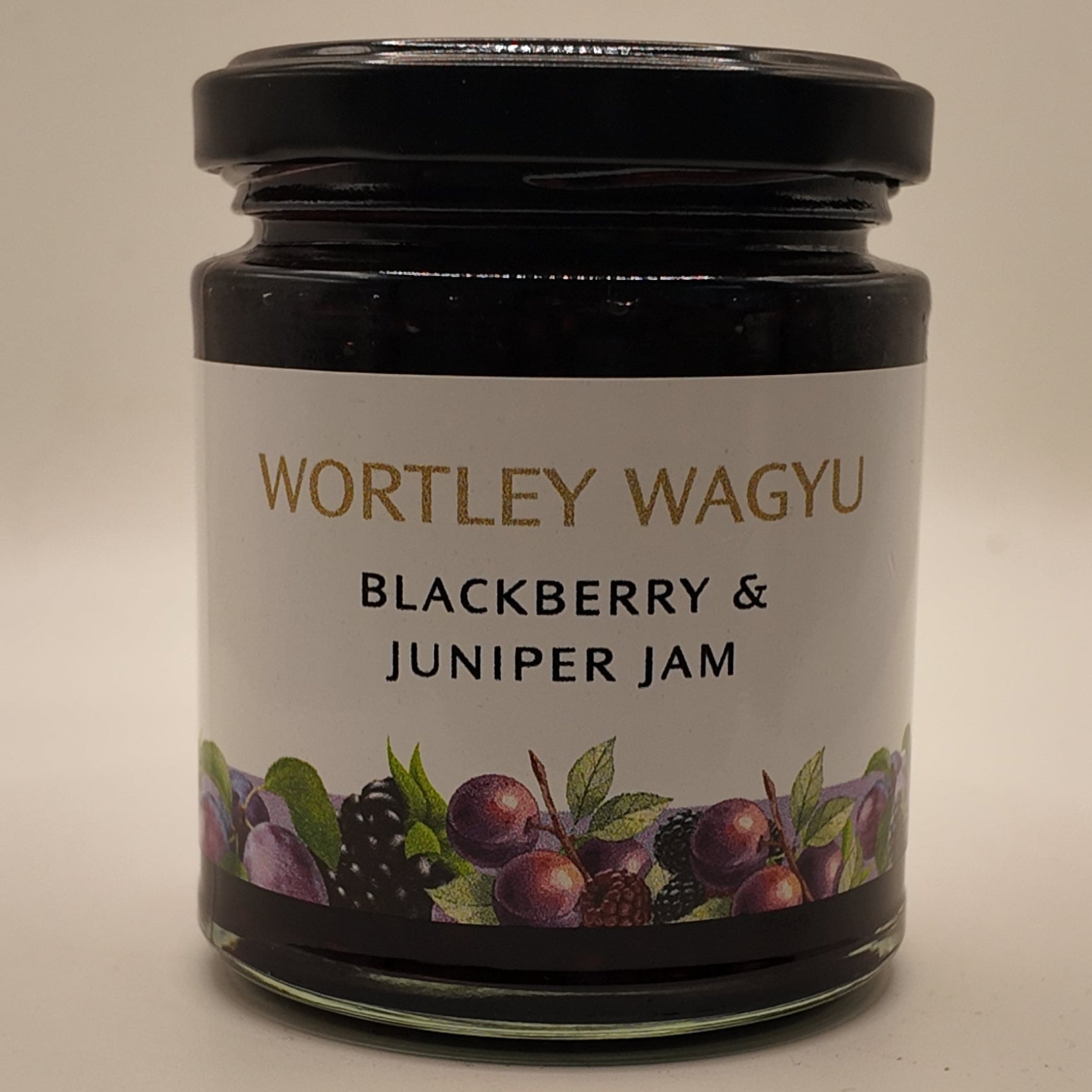 A glass jar of Wortley Wagyu Blackberry & Juniper Jam with a black lid and a white label featuring berry illustrations, set against a plain light background.