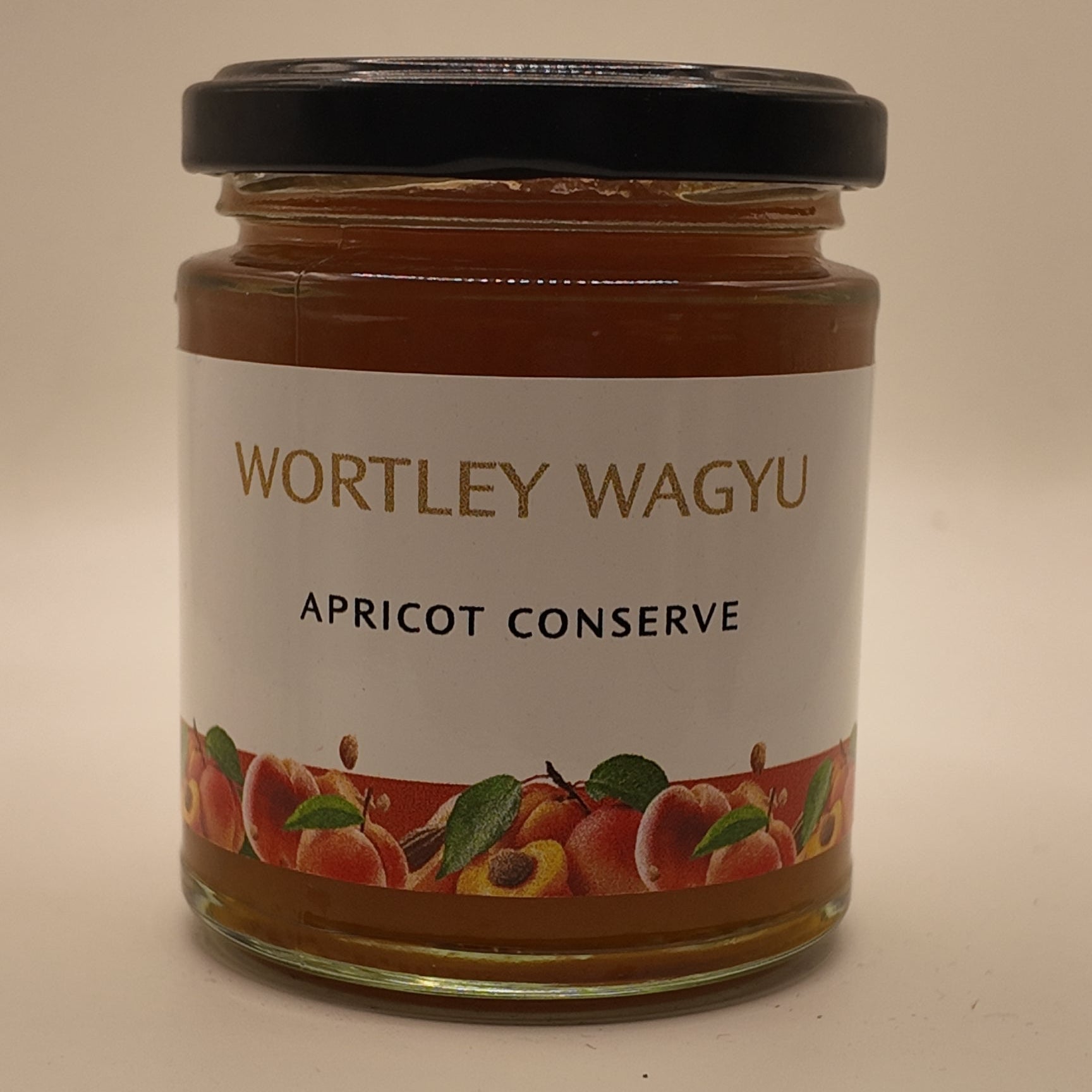 A glass jar of Wortley Wagyu Apricot Conserve with a black lid and a white label featuring red and green apricot illustrations, set against a plain beige background.